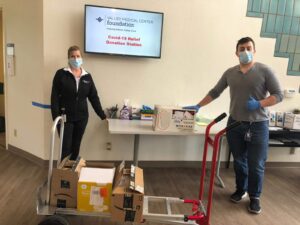 Staff standing next to table and Dolley full of PPE products