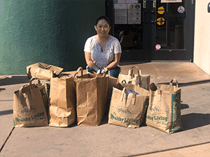 Woman sitting with multiple grocery bags filled with essential supplies.